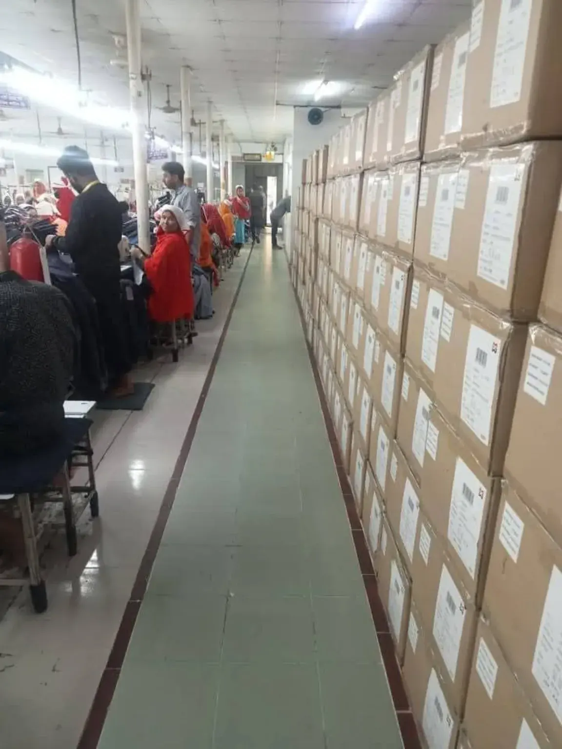 Garment Packing and Carton Storage Aisle A garment packing aisle beside stacked labelled cartons and workers.
