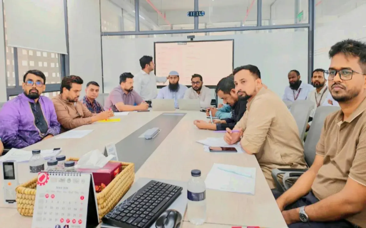 Manufacturing Planning Team Meeting A group seated around a meeting table with notebooks, a laptop and a presentation screen.