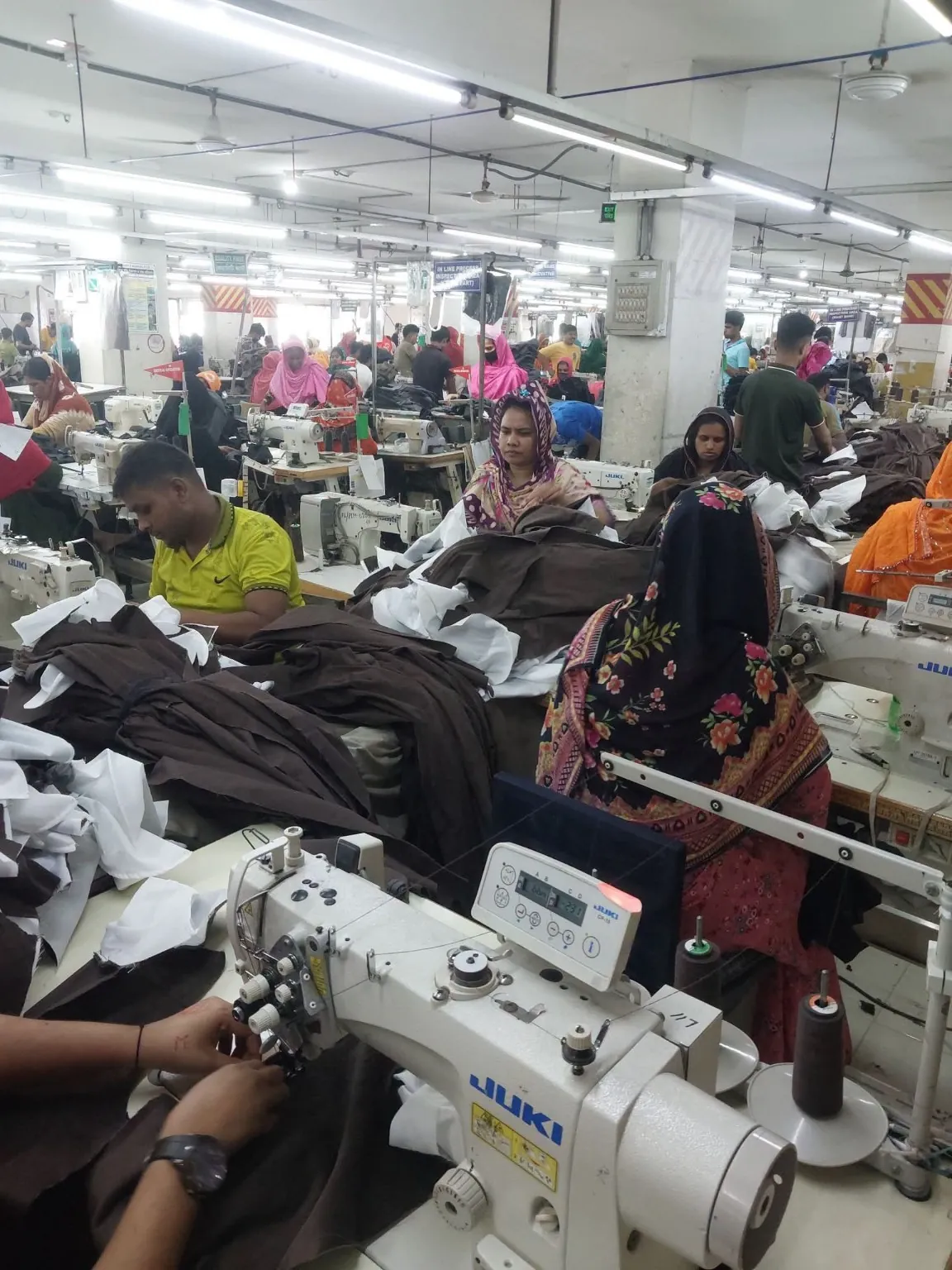 Apparel Assembly with Industrial Sewing Machines Sewing operators assembling brown garment panels across several industrial workstations.