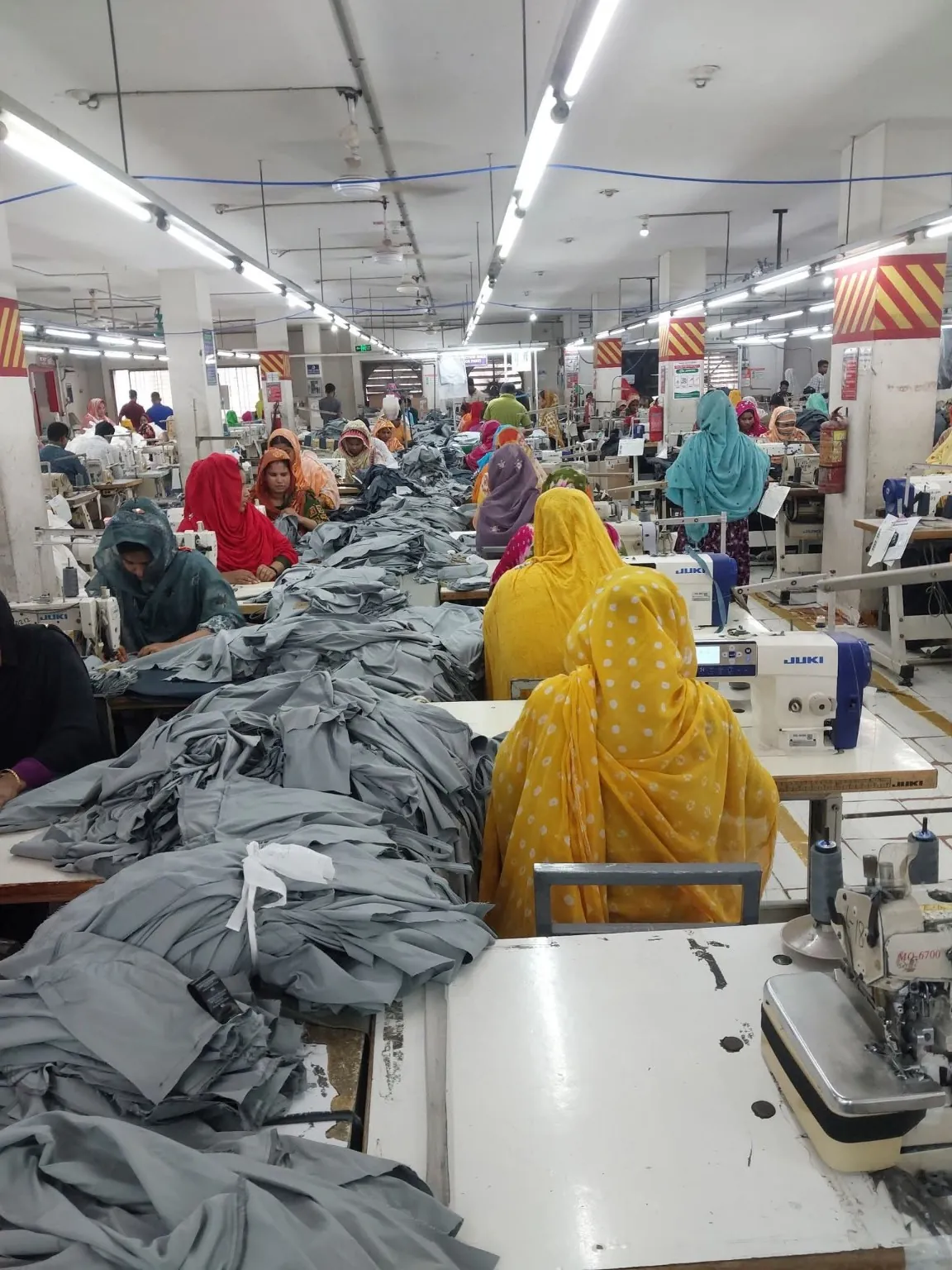 Bulk Garment Production Workstations Rows of sewing workstations with grey garment panels arranged along central tables.