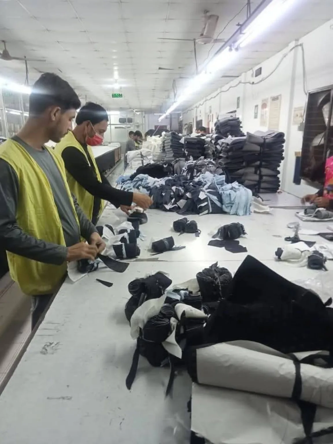 Garment Bundle Sorting and Inspection Workers sorting garment components and bundled fabric on a long inspection table.