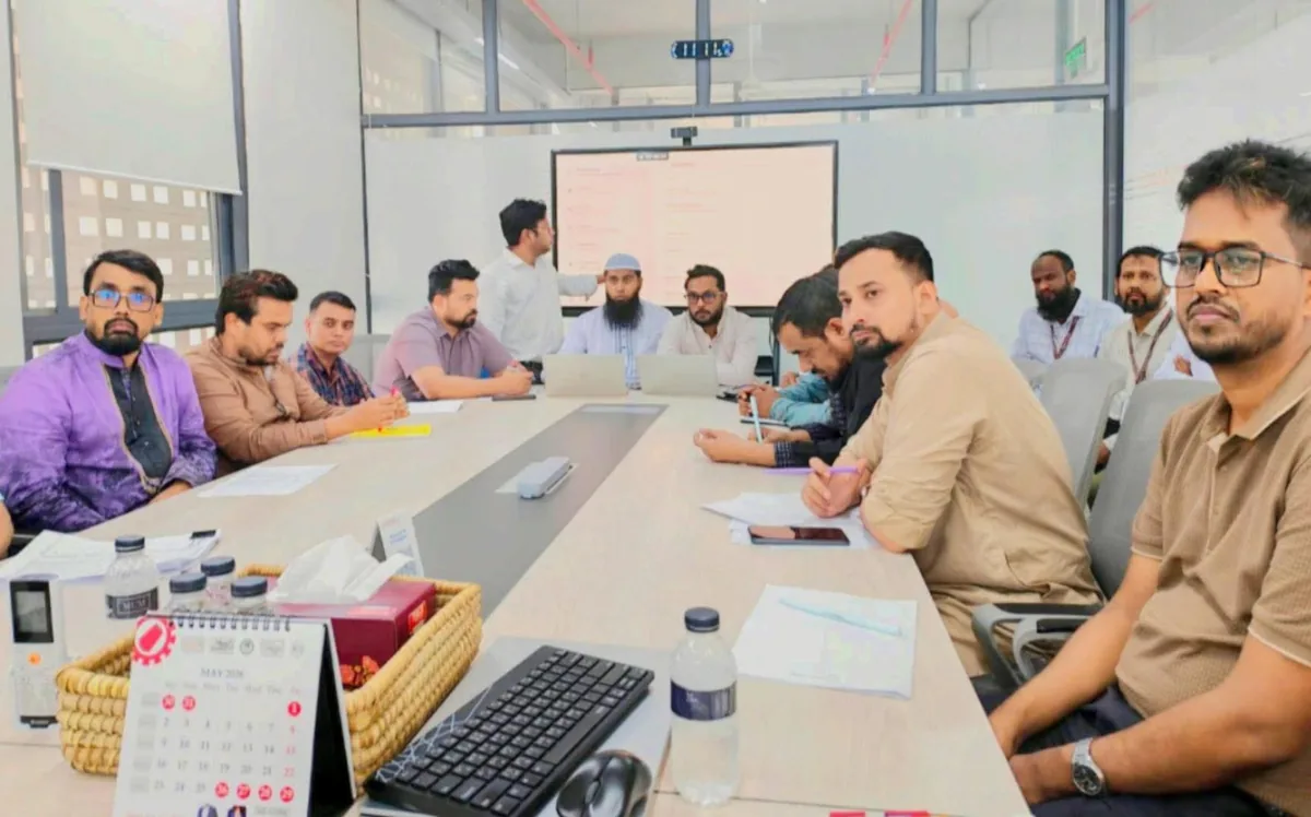 Manufacturing Planning Team Meeting A group seated around a meeting table with notebooks, a laptop and a presentation screen.